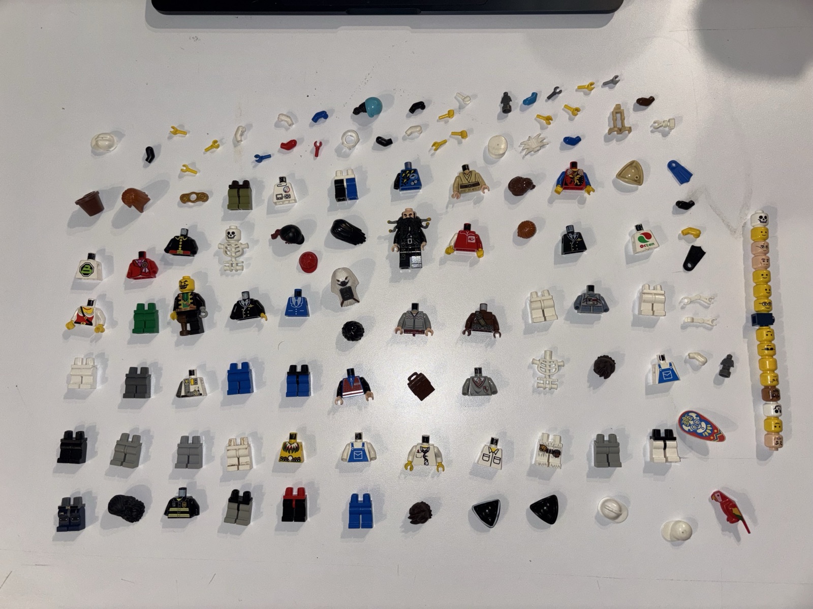 A tray of 127 loose LEGO® minifigure parts and assembled figures spread one layer deep, photographed from above