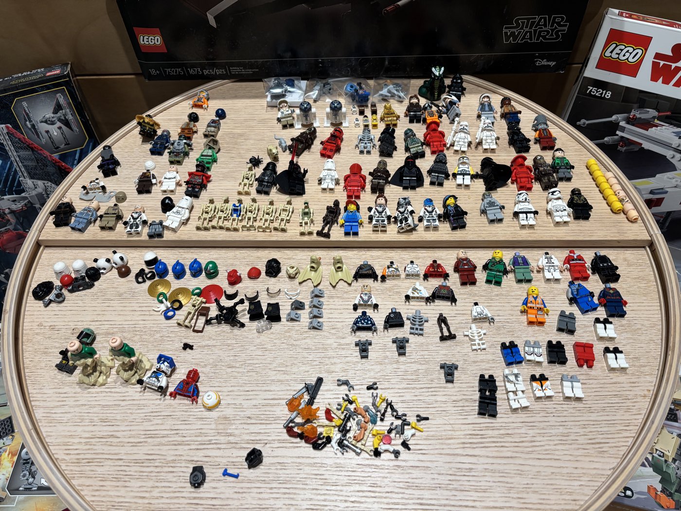 A bulk Star Wars lot mid-identification: rows of assembled minifigures across the top of a round wooden table, with helmets, torsos, and legs sorted into groups below.