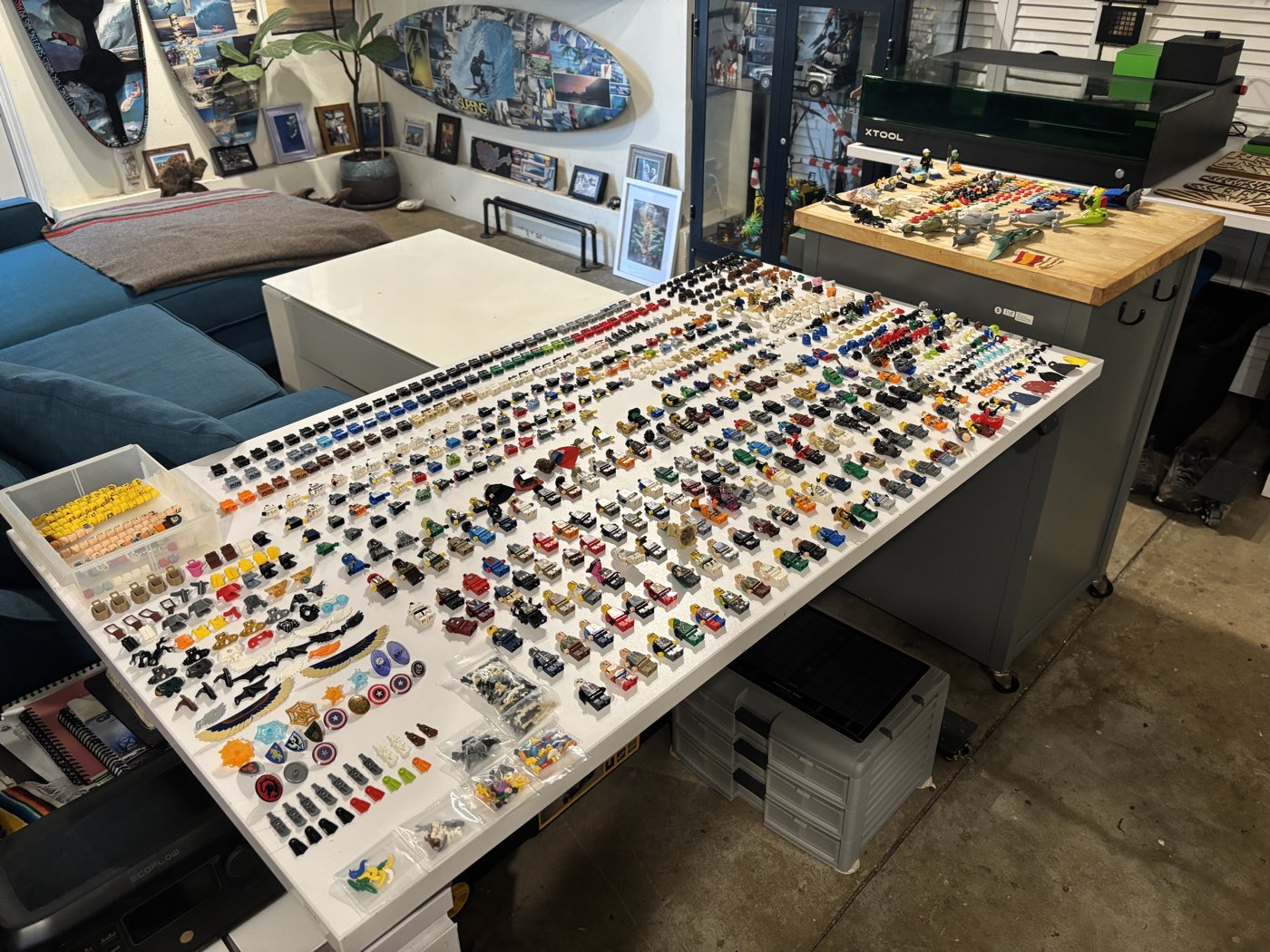 Hundreds of minifigure torsos, legs, headgear, and accessories laid out in meticulous rows across a large white work table for manual identification and completion.