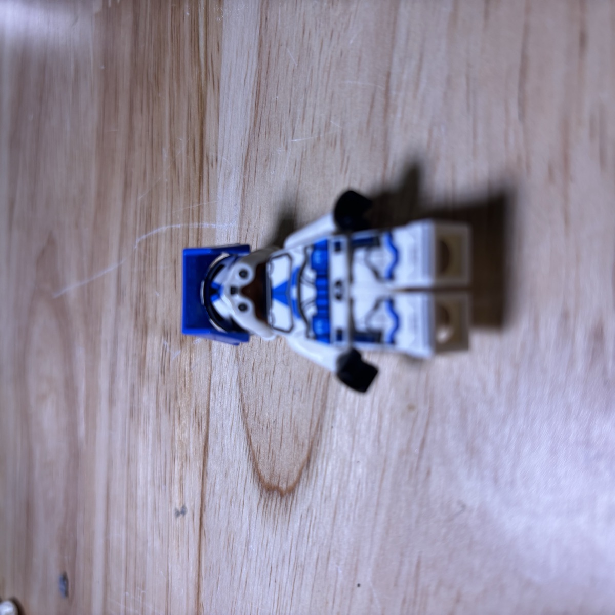 The same LEGO® clone trooper minifigure lying on the desk, photographed low from the feet end so the torso print foreshortens.