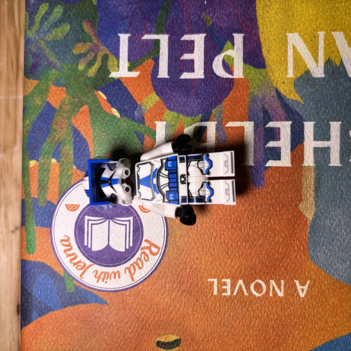 The same LEGO® clone trooper minifigure lying on a brightly patterned printed book cover.