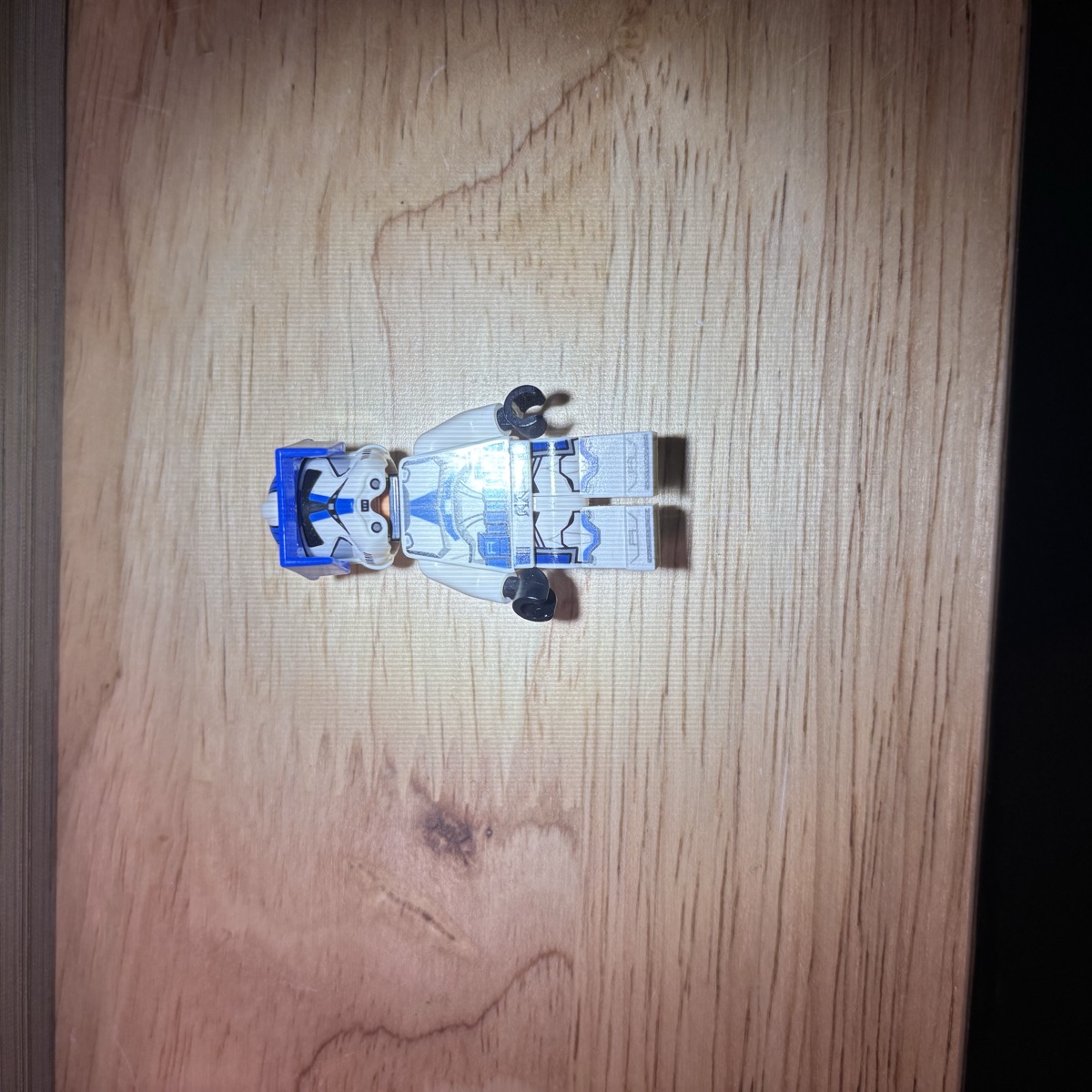 The same LEGO® clone trooper minifigure on a wooden desk with a desk-lamp hot spot washing out the torso print.