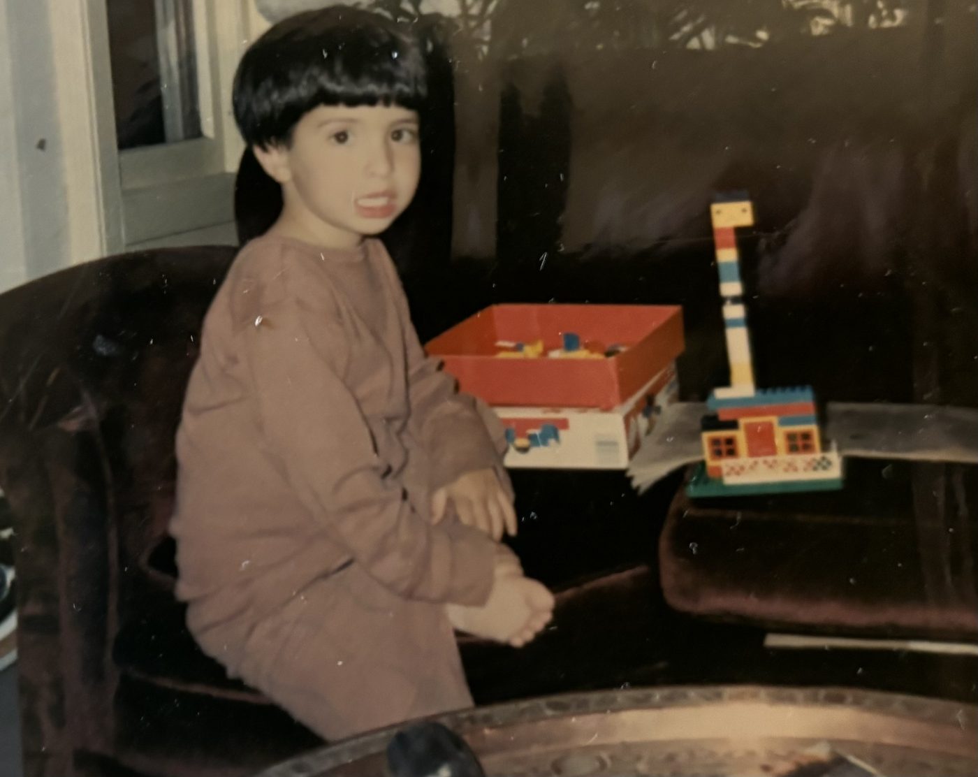 Preschool-age me on the couch with the Basic Builder Set — the box open beside me and a little tower build on the armrest.