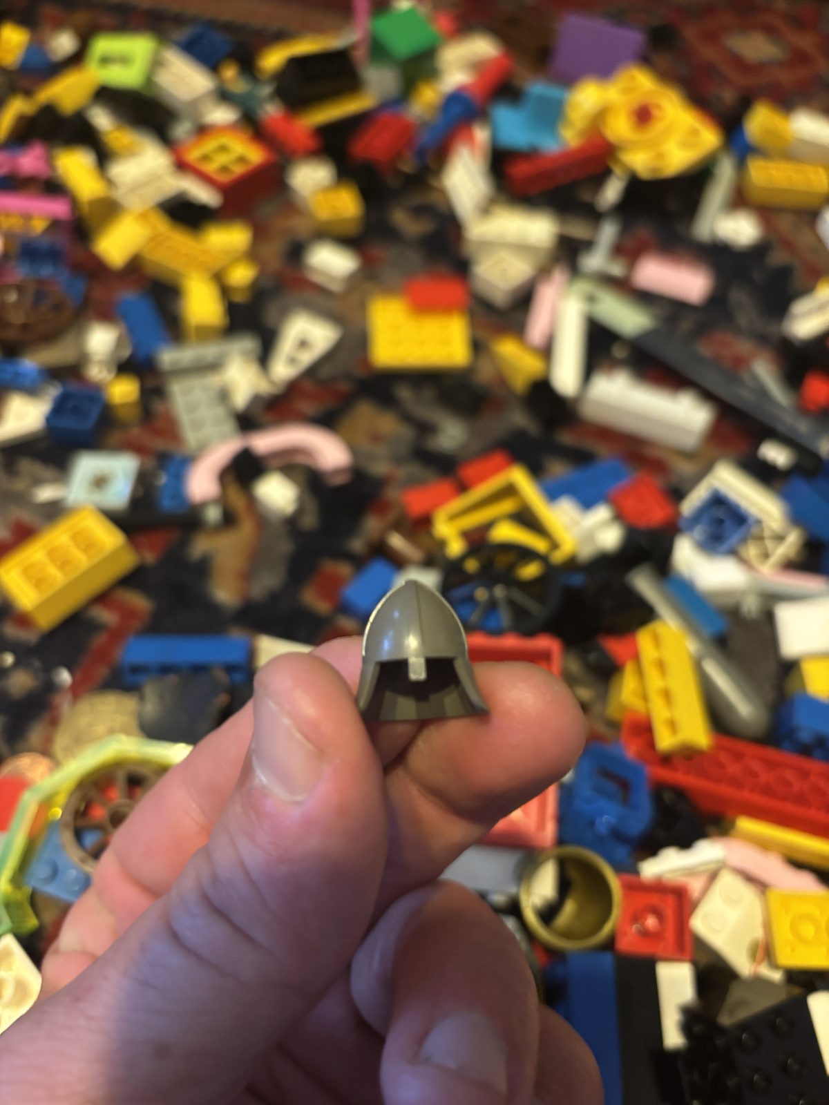 A grey knight's helmet held up over the spread of loose bricks on the rug.